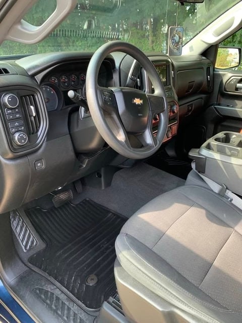 Interior of Chevrolet truck showing steering wheel, dashboard, and front seats with view through windshield to grassy outdoor setting