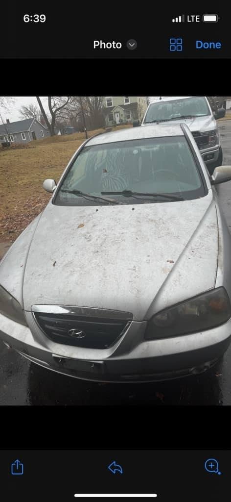 White Hyundai sedan parked in driveway covered with dirt and grime, residential neighborhood in background