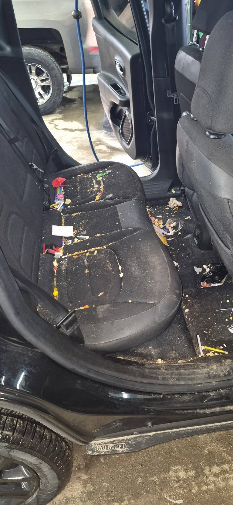 Interior of car with open door showing dirty black seat covered with debris and scattered items