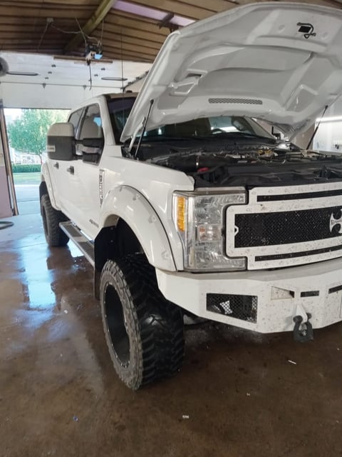 White Ford pickup truck in garage with open hood displaying engine, wet floor visible beneath vehicle