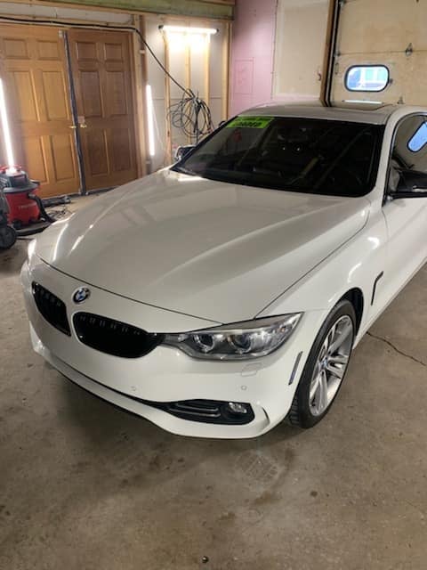 White BMW 4 Series parked in an indoor garage with wooden doors and concrete floor